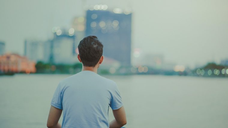 Photo of Man Wearing Blue Shirt Sitting Looking on High-rise Buildings