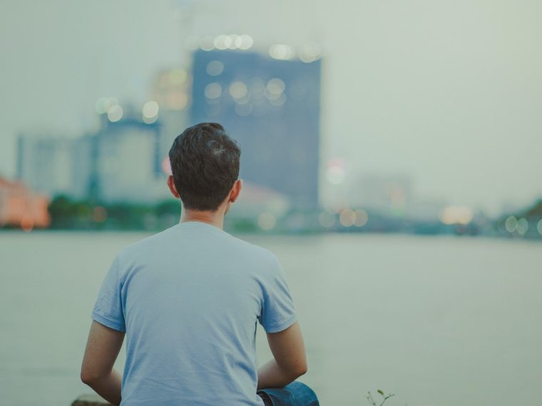 Photo of Man Wearing Blue Shirt Sitting Looking on High-rise Buildings