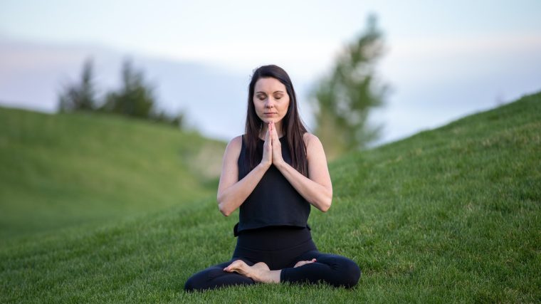 woman in black tank top and black pants sitting on green grass field during daytime